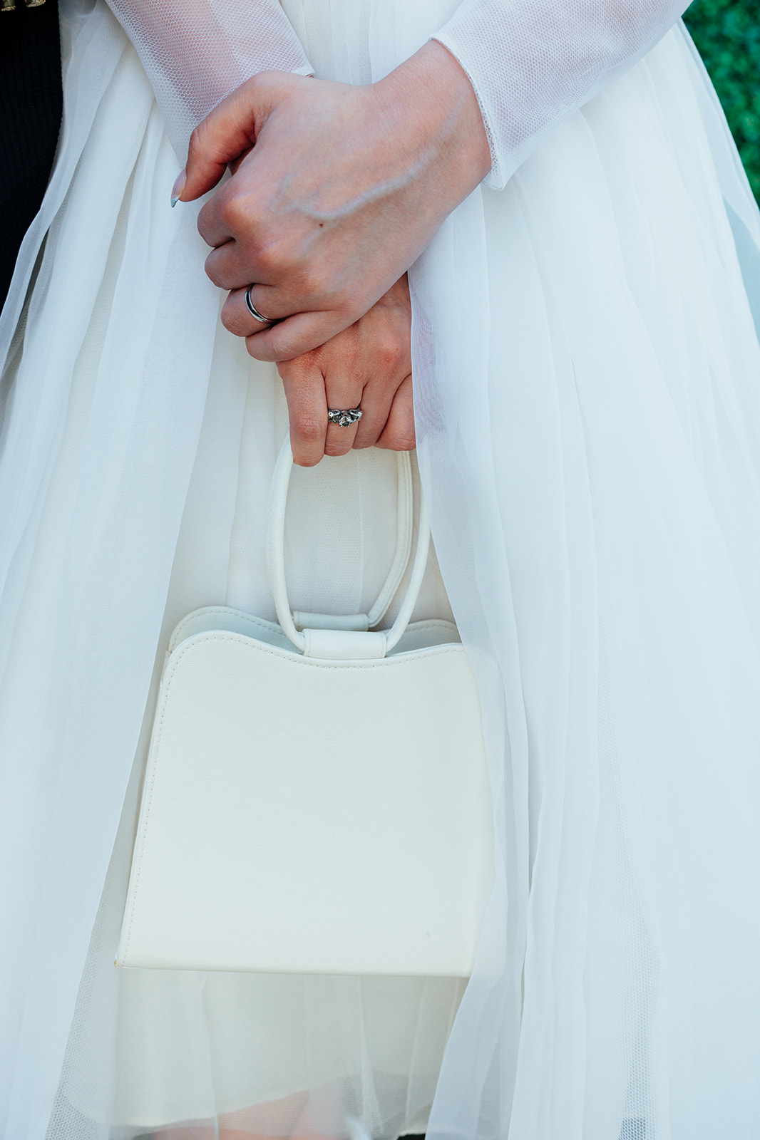 Close-up of bride’s hands showing wedding ring and elegant white handbag