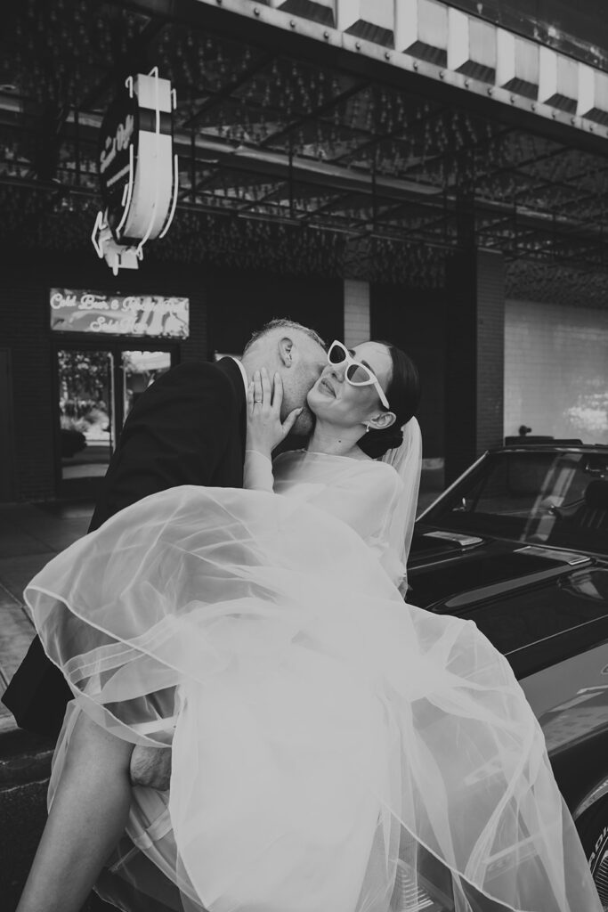 Black-and-white photo of bride and groom embracing by a vintage car in Las Vegas