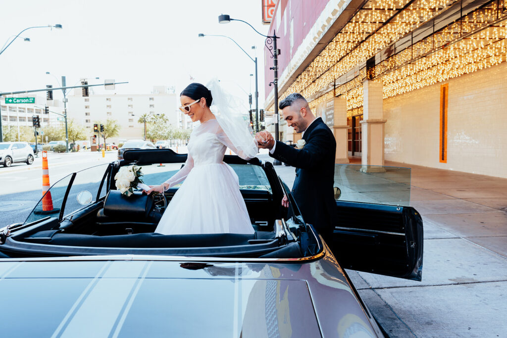 Bride and groom stepping into a classic convertible car outside Plaza Hotel in Las Vegas