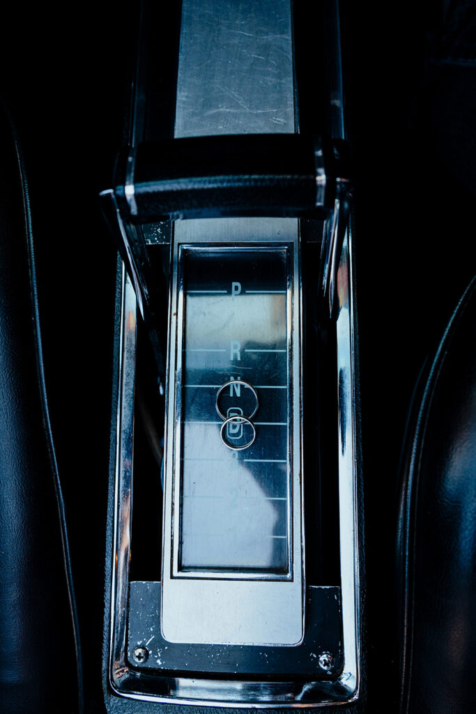 Close-up of wedding rings placed on a vintage car’s gear shifter outside Plaza Hotel