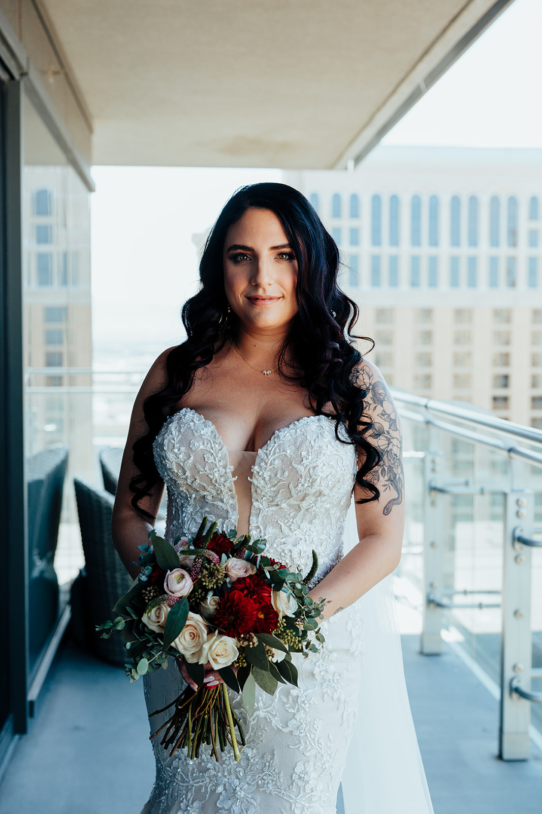 Bride in lace wedding gown holding bouquet of roses on a hotel balcony