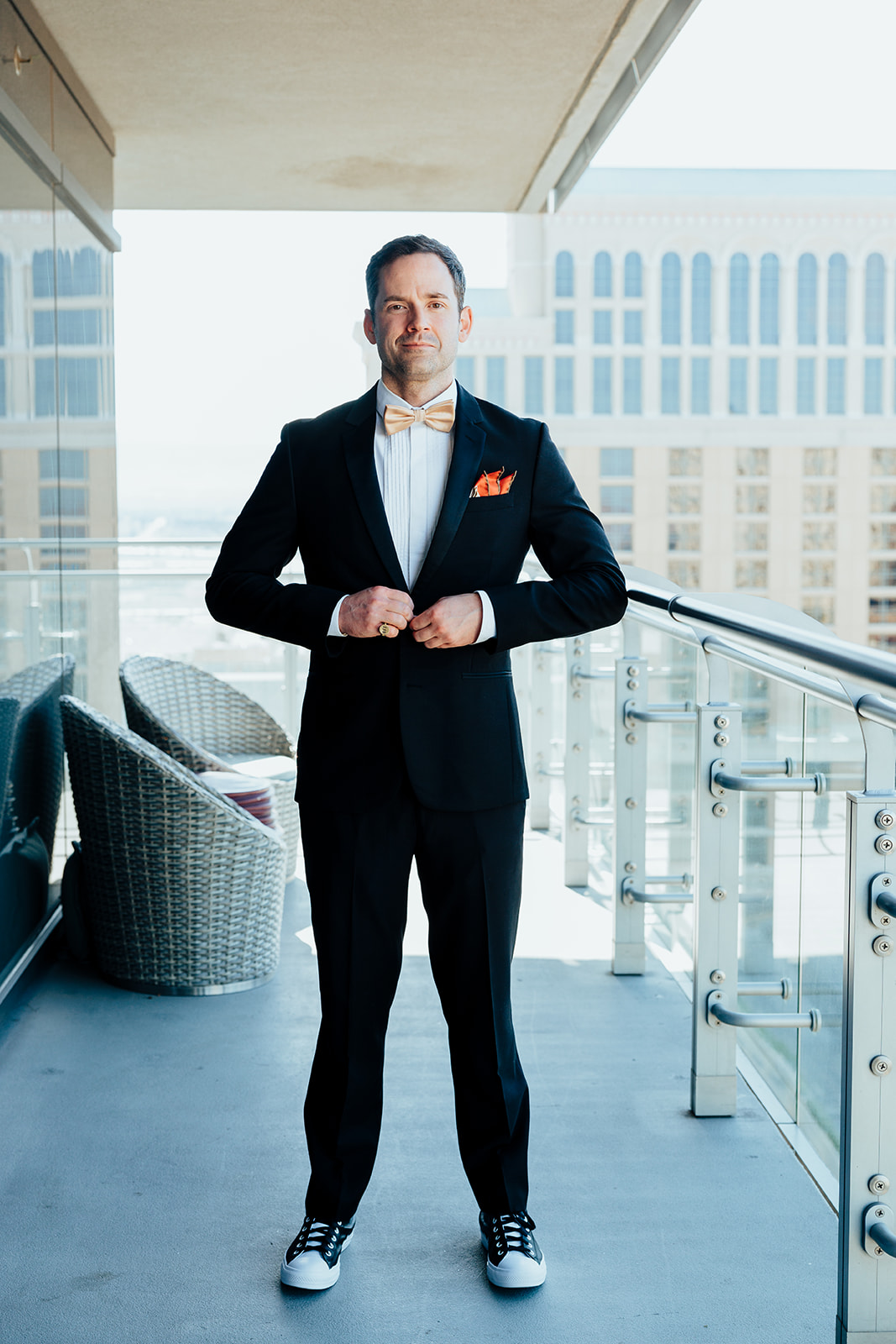 Groom posing on hotel balcony in Las Vegas wearing tuxedo and gold bow tie