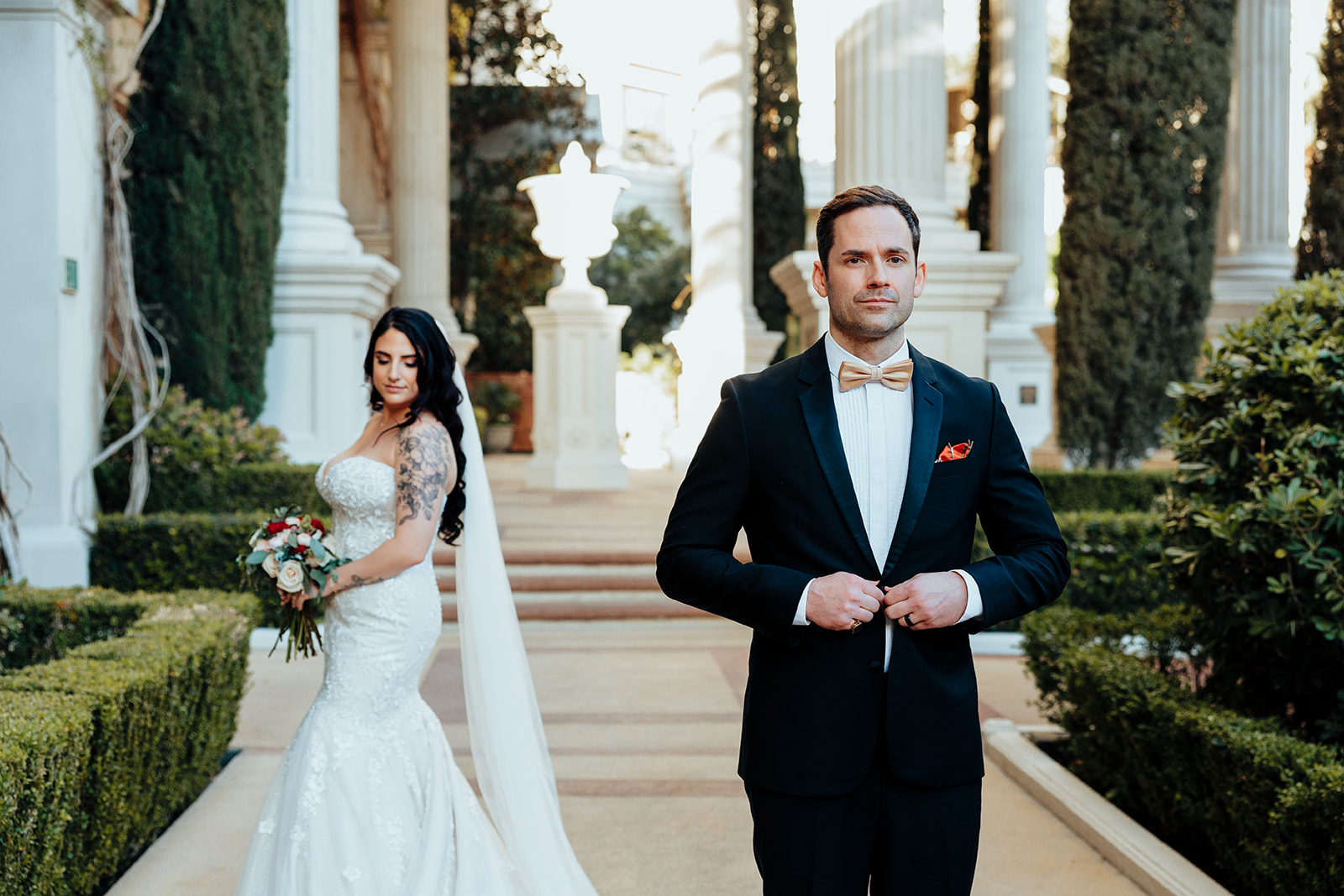 Groom adjusts tuxedo as bride poses with bouquet in Juno Garden