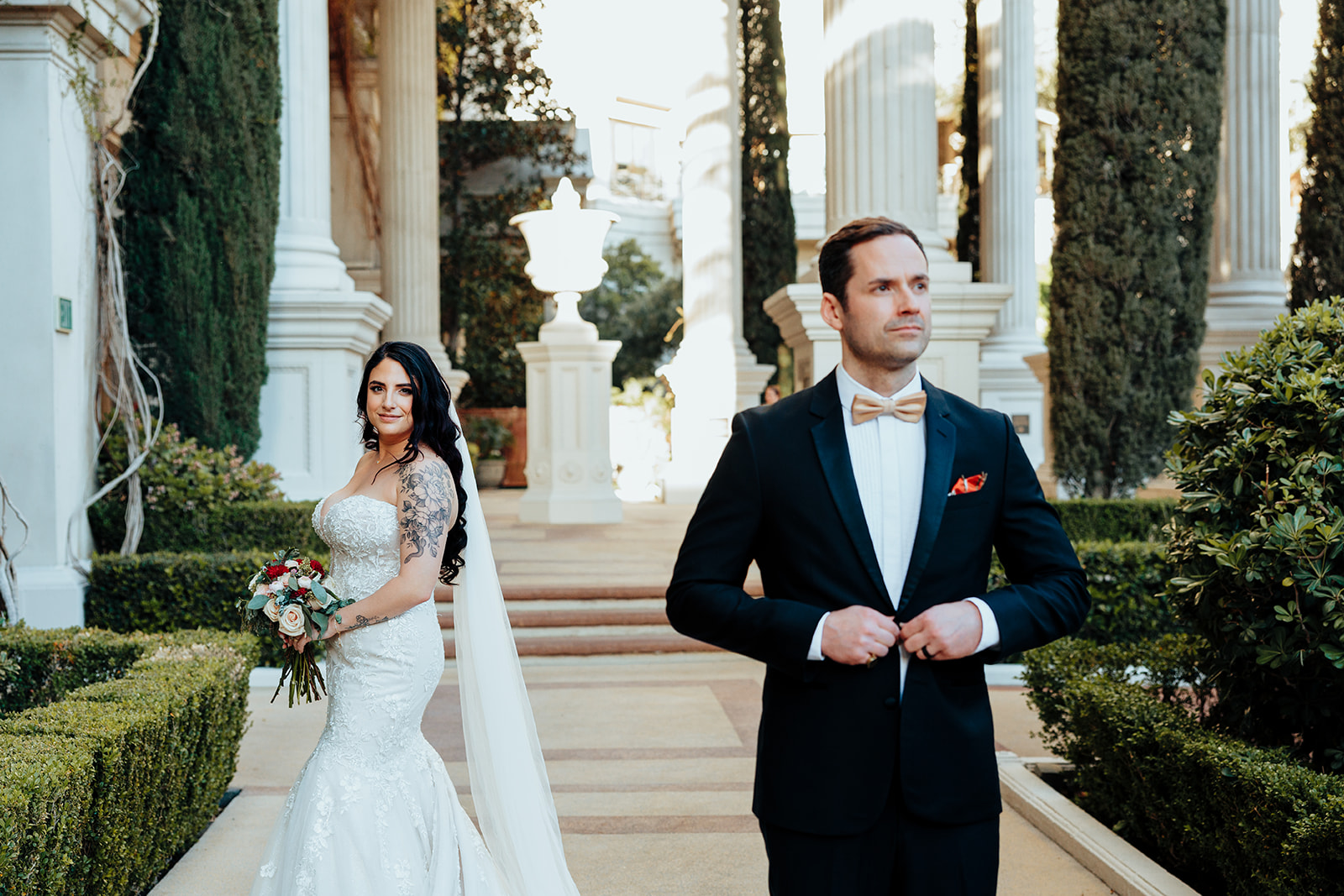 Groom adjusting suit as bride smiles in Juno Garden at Caesars Palace