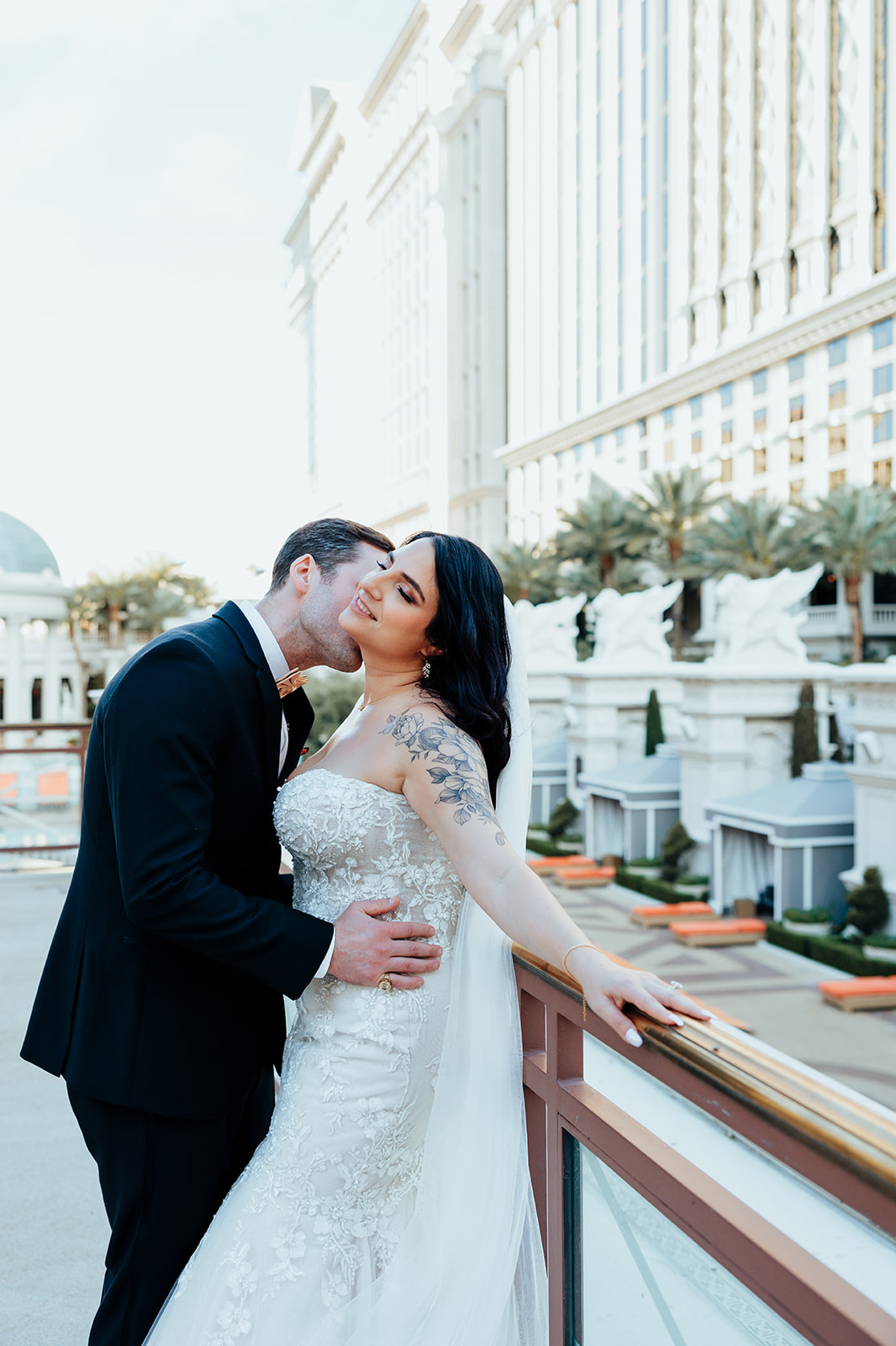 Groom kissing bride on balcony at Caesars Palace with elegant backdrop