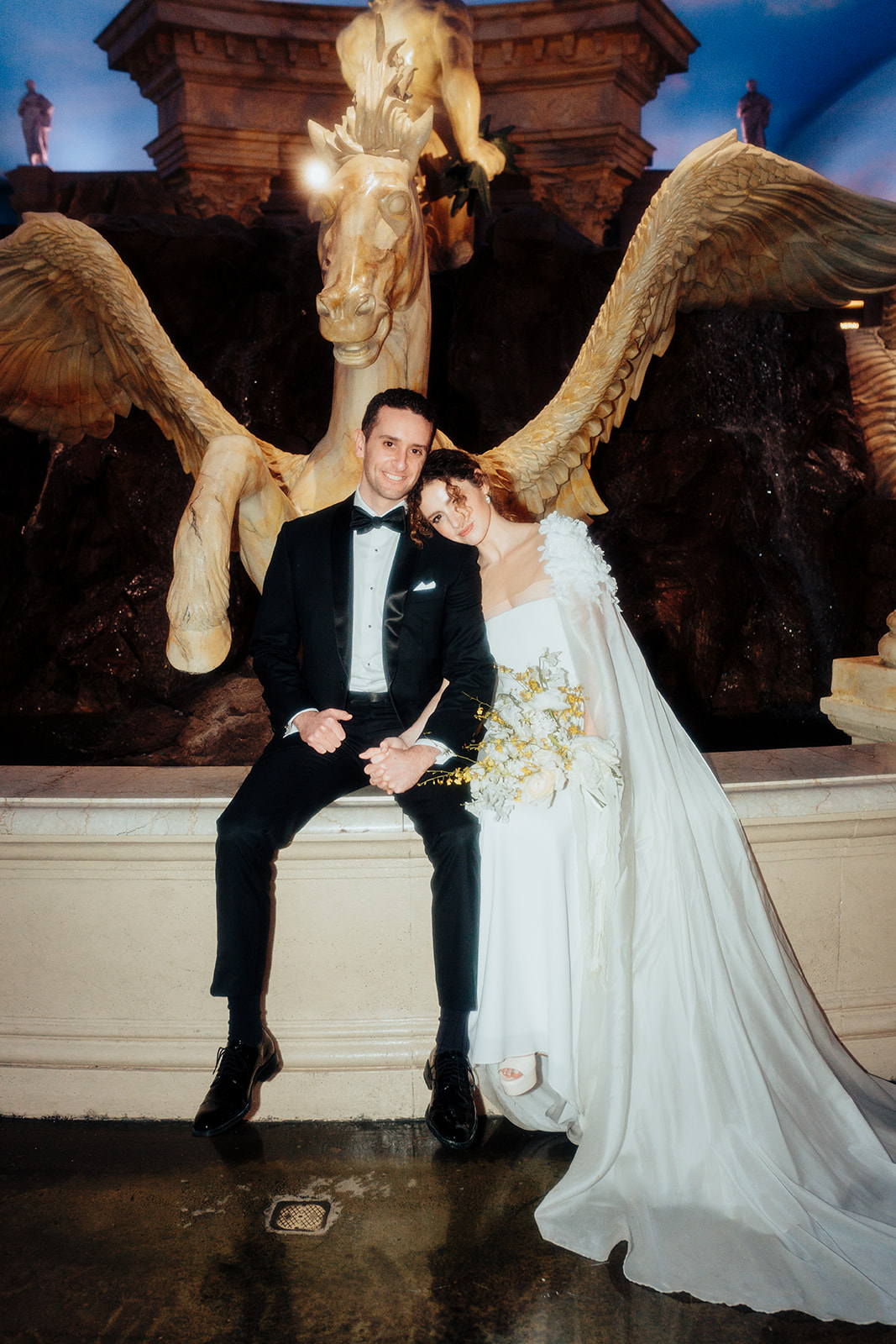 Bride and groom posing together in front of a grand fountain at Caesars Palace during their Las Vegas wedding celebration.