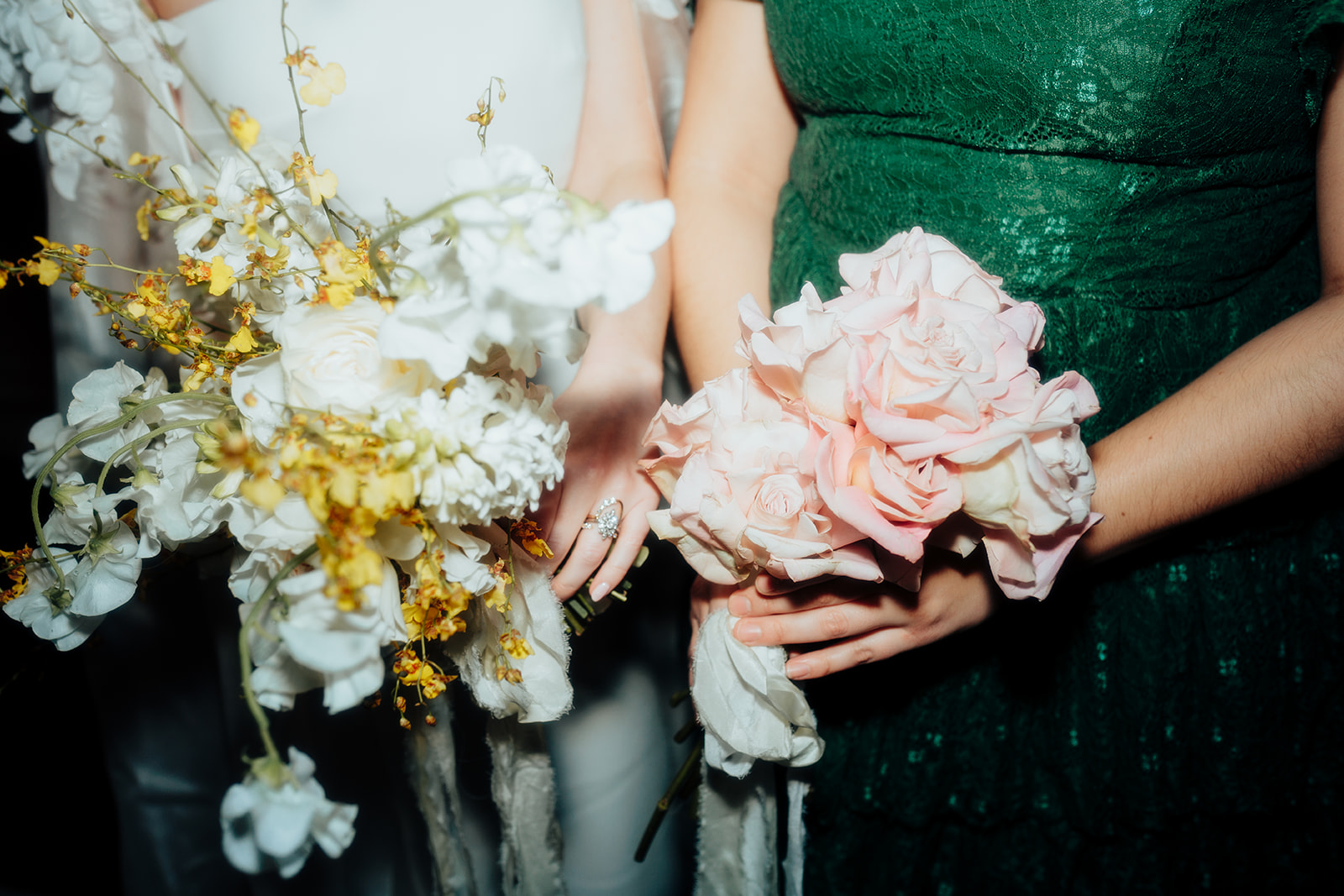 Close-up of a bride and bridesmaid holding bouquets featuring white and yellow flowers and pink roses during a Las Vegas winter wedding celebration.