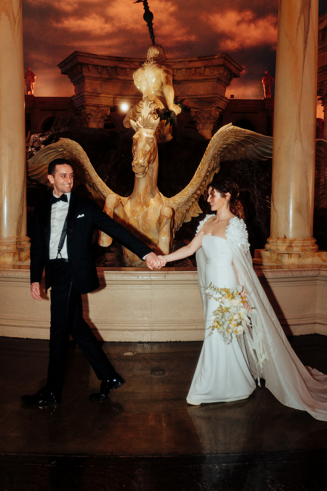 Bride and groom holding hands while walking near the iconic fountain at Caesars Palace during their Las Vegas winter wedding celebration