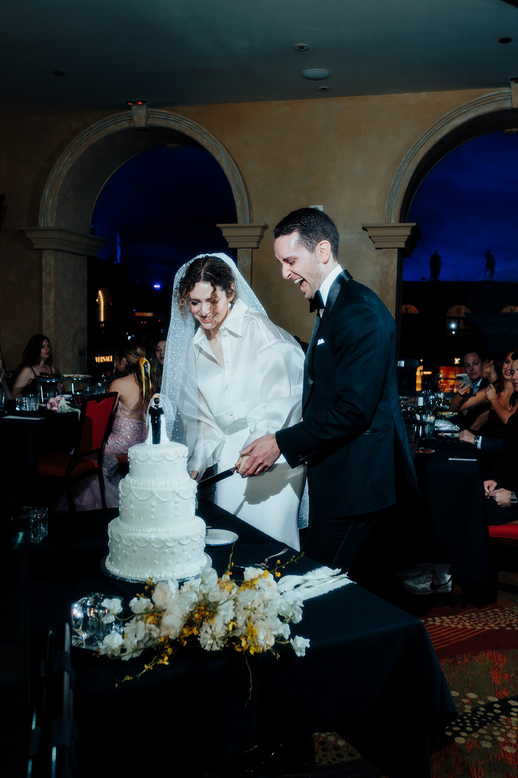 Bride and groom joyfully cutting their wedding cake at the reception in Caesars Palace during their Las Vegas wedding celebration.