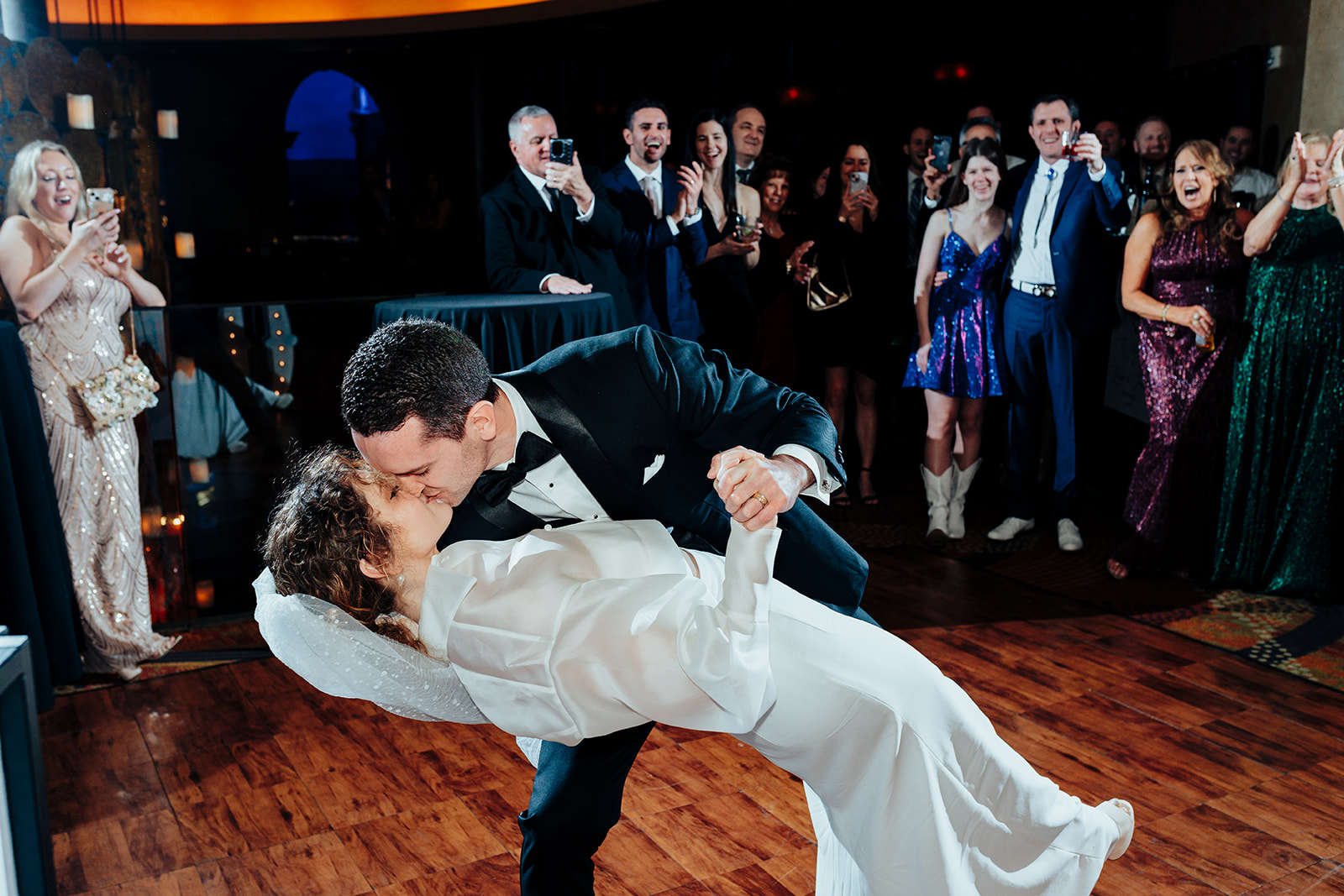 The groom dips the bride for a romantic kiss during their first dance on the dance floor, surrounded by cheering guests at their Las Vegas wedding reception at Caesars Palace.