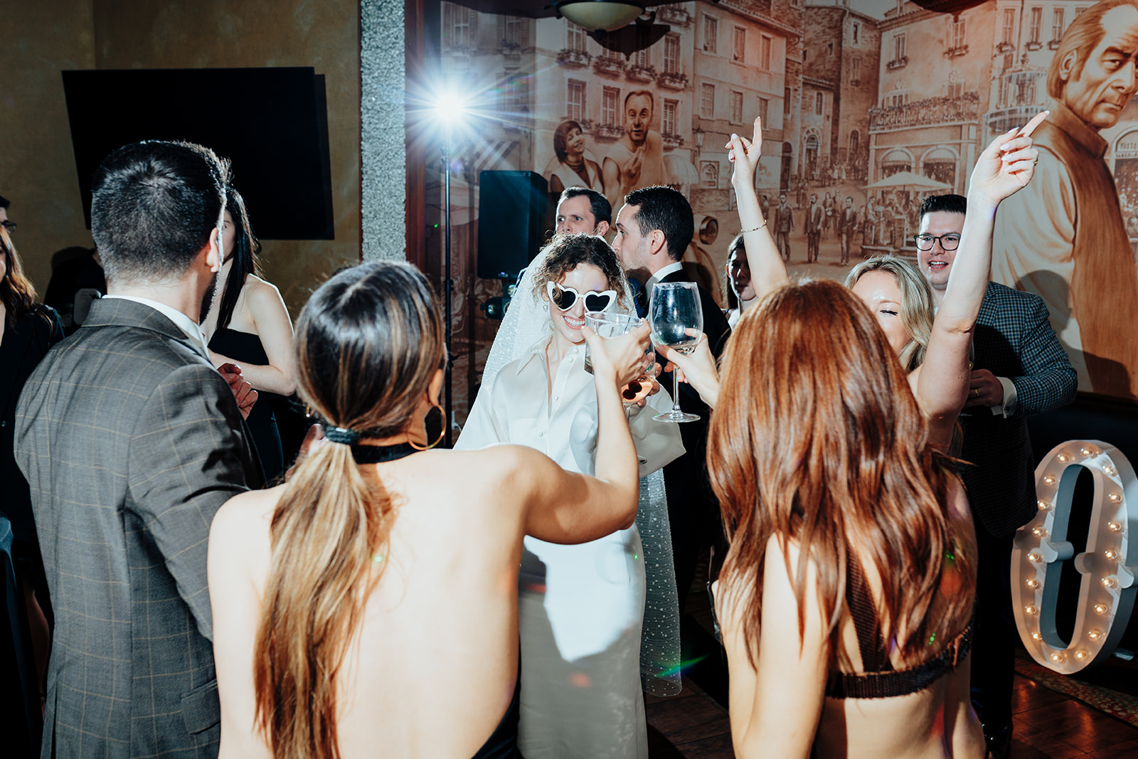 Bride wearing heart-shaped sunglasses raising a toast with guests during a lively wedding celebration at Caesars Palace in Las Vegas.