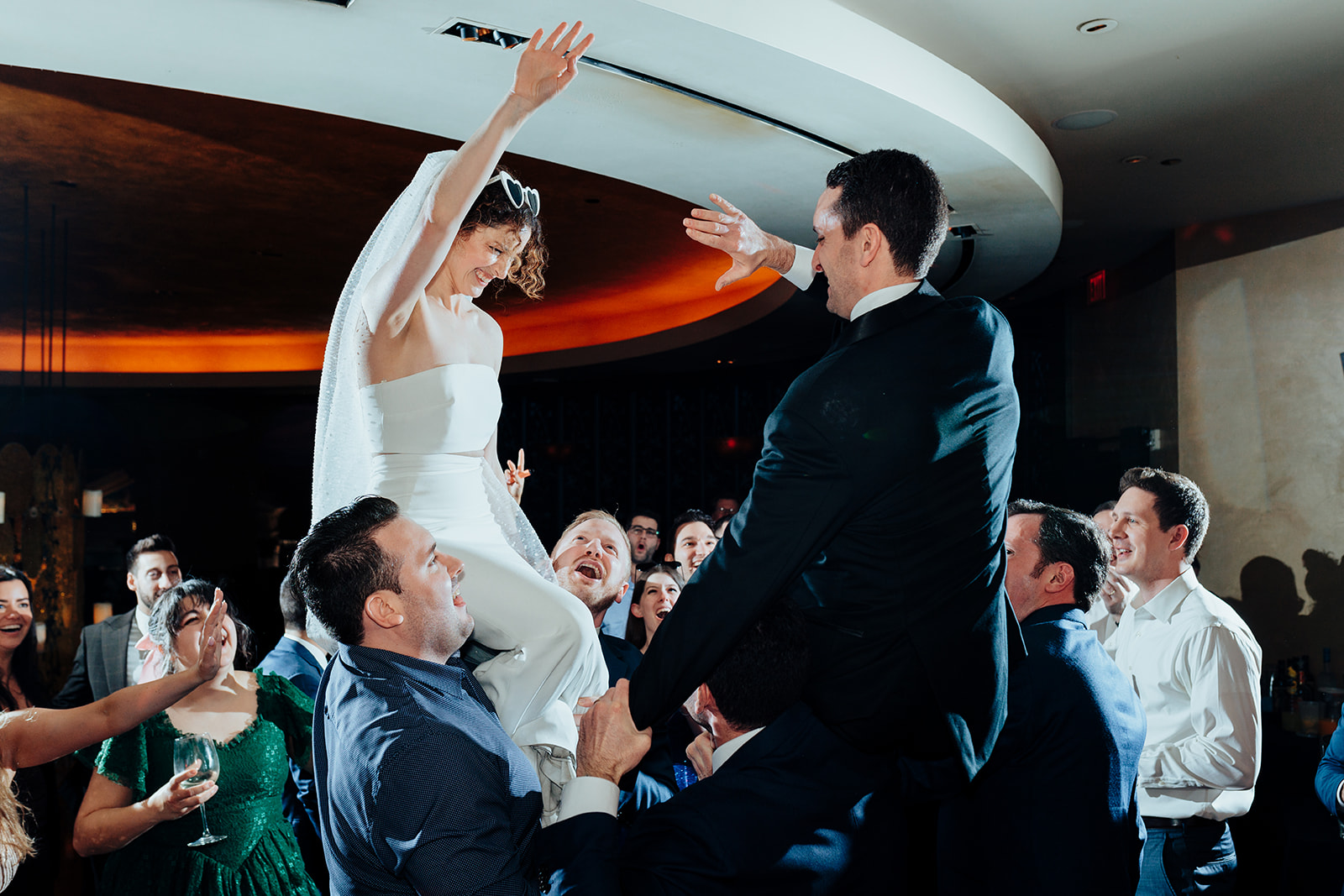 Bride and groom raised on chairs by guests during a lively wedding celebration at their Las Vegas reception at Caesars Palace.