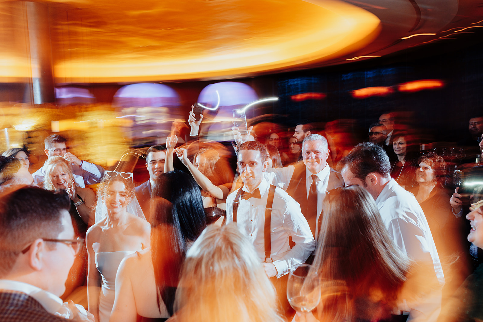 Bride and groom surrounded by guests on the dance floor with vibrant lights and motion blur capturing the festive atmosphere of a Las Vegas wedding reception.