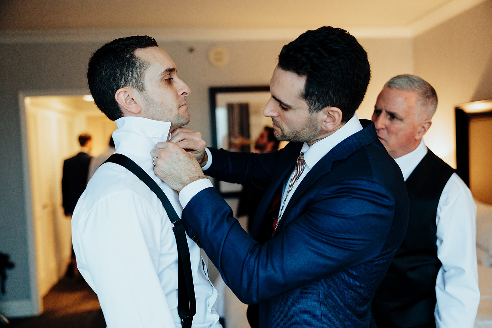 Groom being assisted by his groomsman to adjust his shirt collar indoors, preparing for the Vegas Winter Wedding ceremony.