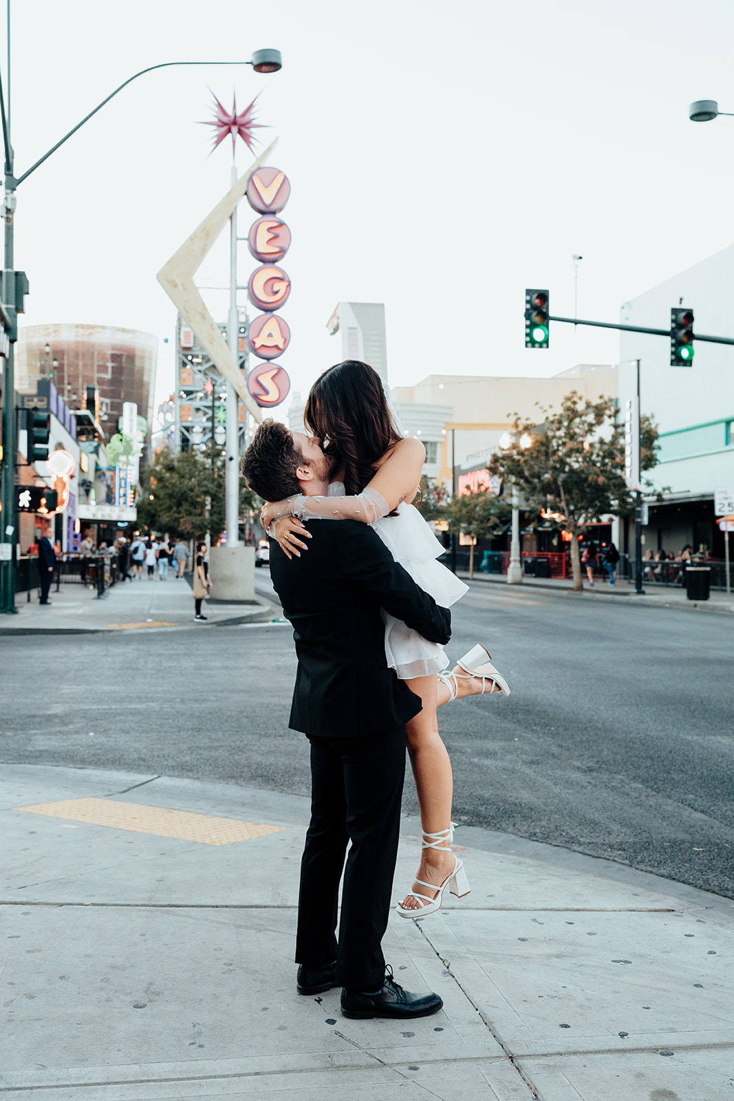 Groom lifting his bride in the middle of a city street, sharing a romantic kiss with the iconic Vegas sign in the background.