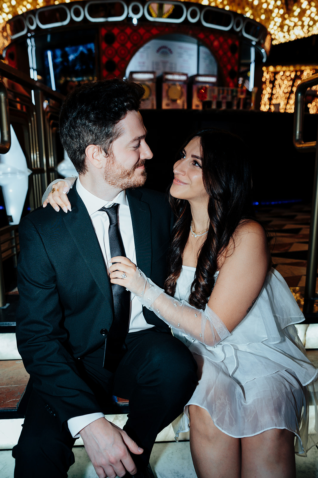 Engaged couple sitting on stairs, gazing lovingly at each other with a vintage-inspired casino backdrop.