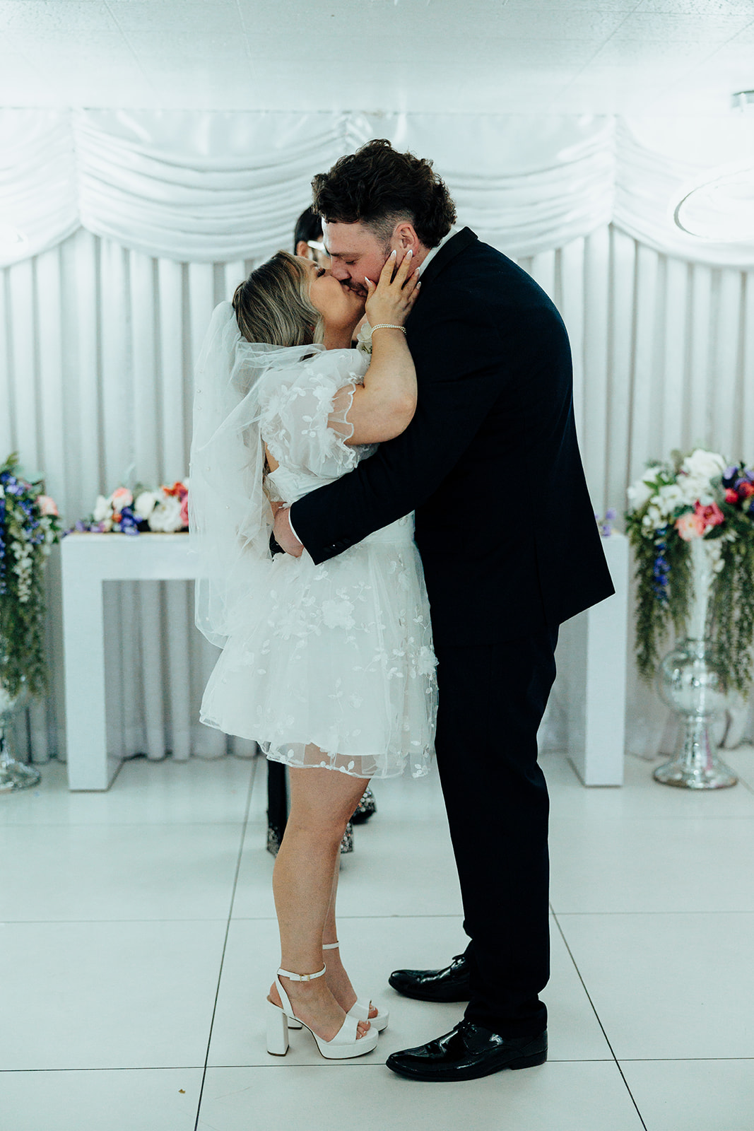 Bride and groom sharing their first kiss at Little White Wedding Chapel elopement, with white drapes and floral decor in the background.