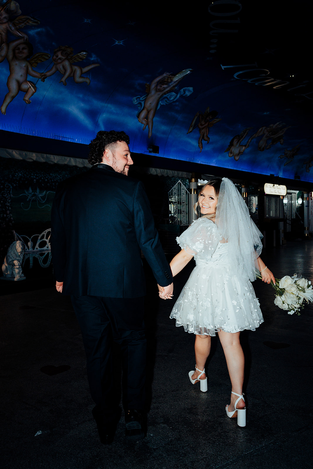 Bride and groom walking hand in hand after elopement at Little White Wedding Chapel, with Las Vegas street signs and night sky in the background.