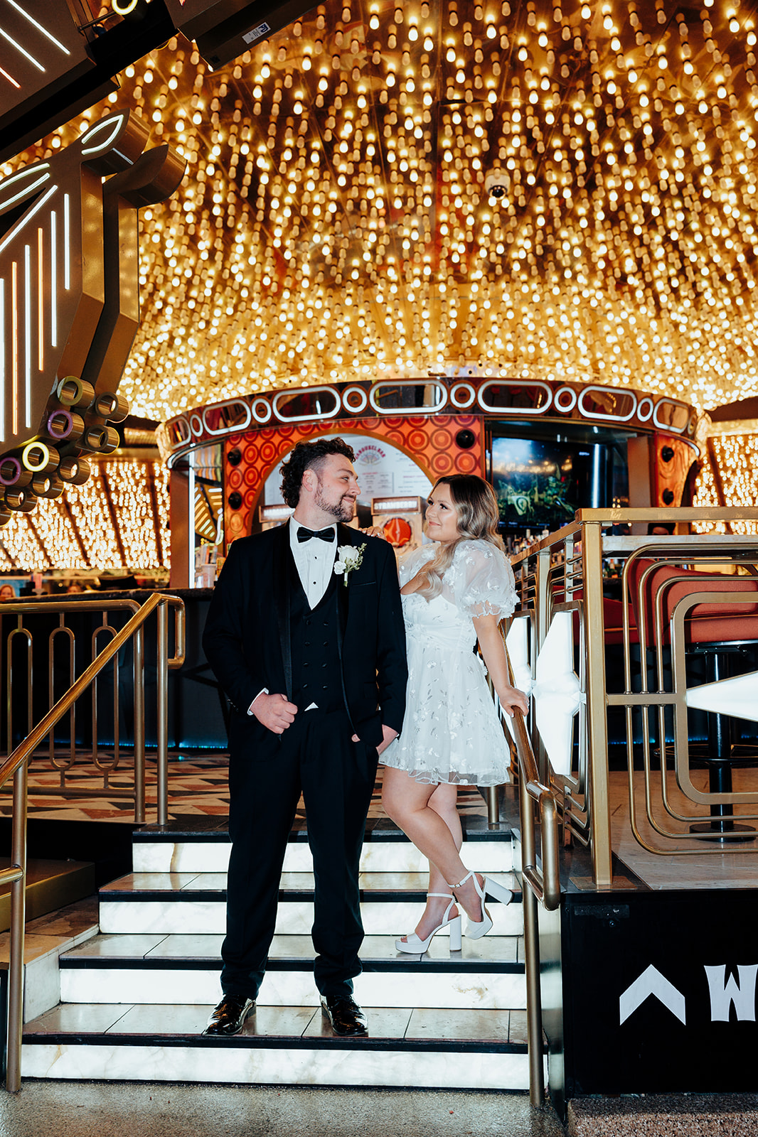 Bride and groom posing on staircase on Las Vegas Strip after Little White Wedding Chapel elopement, with bright ceiling lights in the background.