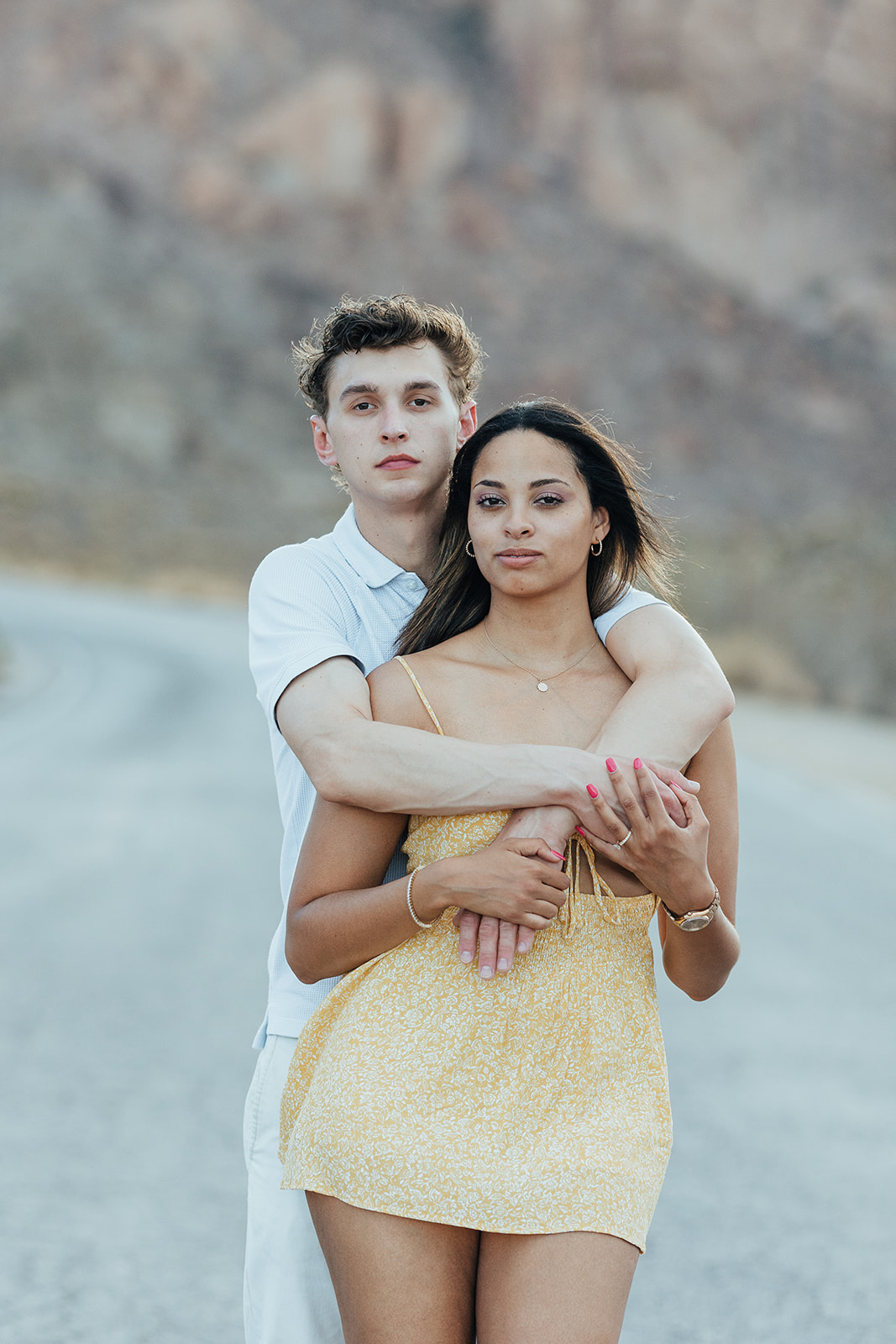A couple shares a warm embrace on a deserted road at Nelson's Ghost Town, with rugged desert cliffs in the background, capturing an intimate wedding proposal moment.