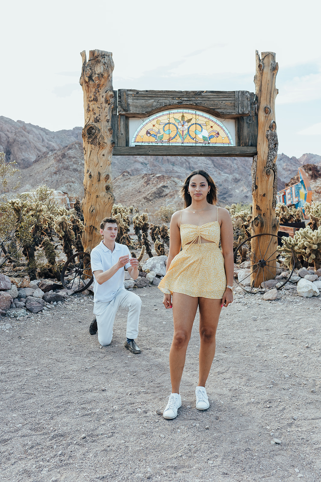 A person proposing on one knee under a stained glass arch at Nelson's Ghost Town, Nevada, surrounded by cacti and desert mountains.