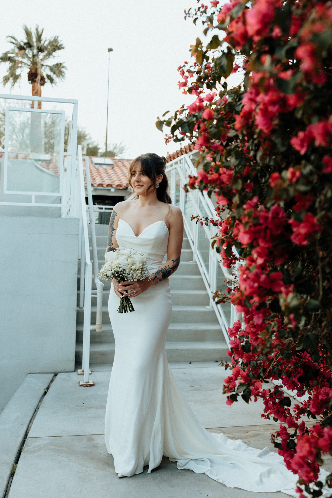 The Bride outside, next to a bunch of red flowers, preparing for her Wedding
